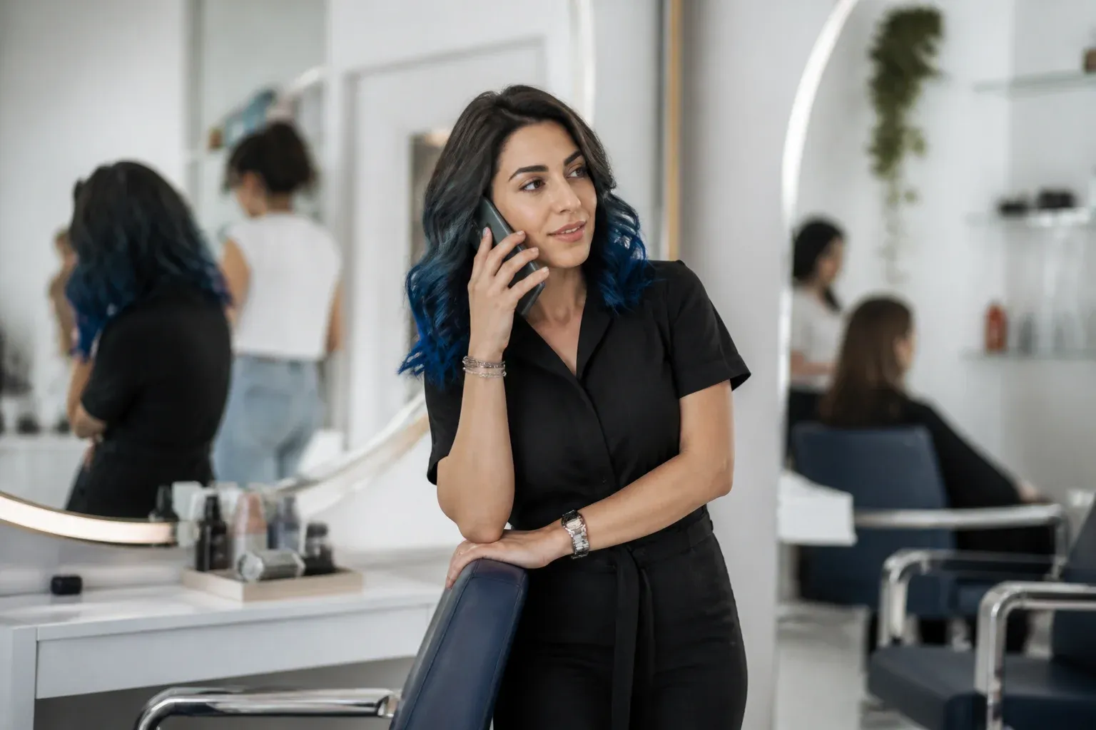 בעלת מכון יופי עם שיער צבעוני משוחחת בטלפון ליד המראה